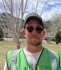 Park Maintenance Assistant, Tim Baca.  Man with reflective vest and glasses, standing in park.